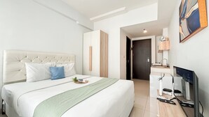 A modern hotel room with a large bed, a desk with a computer, and a door leading to a bathroom.