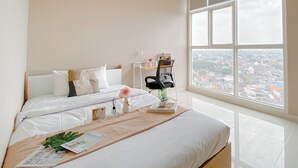 A hotel room with a large window, a bed with white linens, a bedside table with a lamp, a chair, and a view of the city. - Good Deal and New Furnished 2BR Ciputra International Apartment (Jakarta)