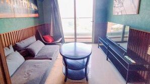 A modern living room with a sofa, a round table, a TV, and a large window. - Wonderful Thematic 2BR at Praxis Apartment (Surabaya)