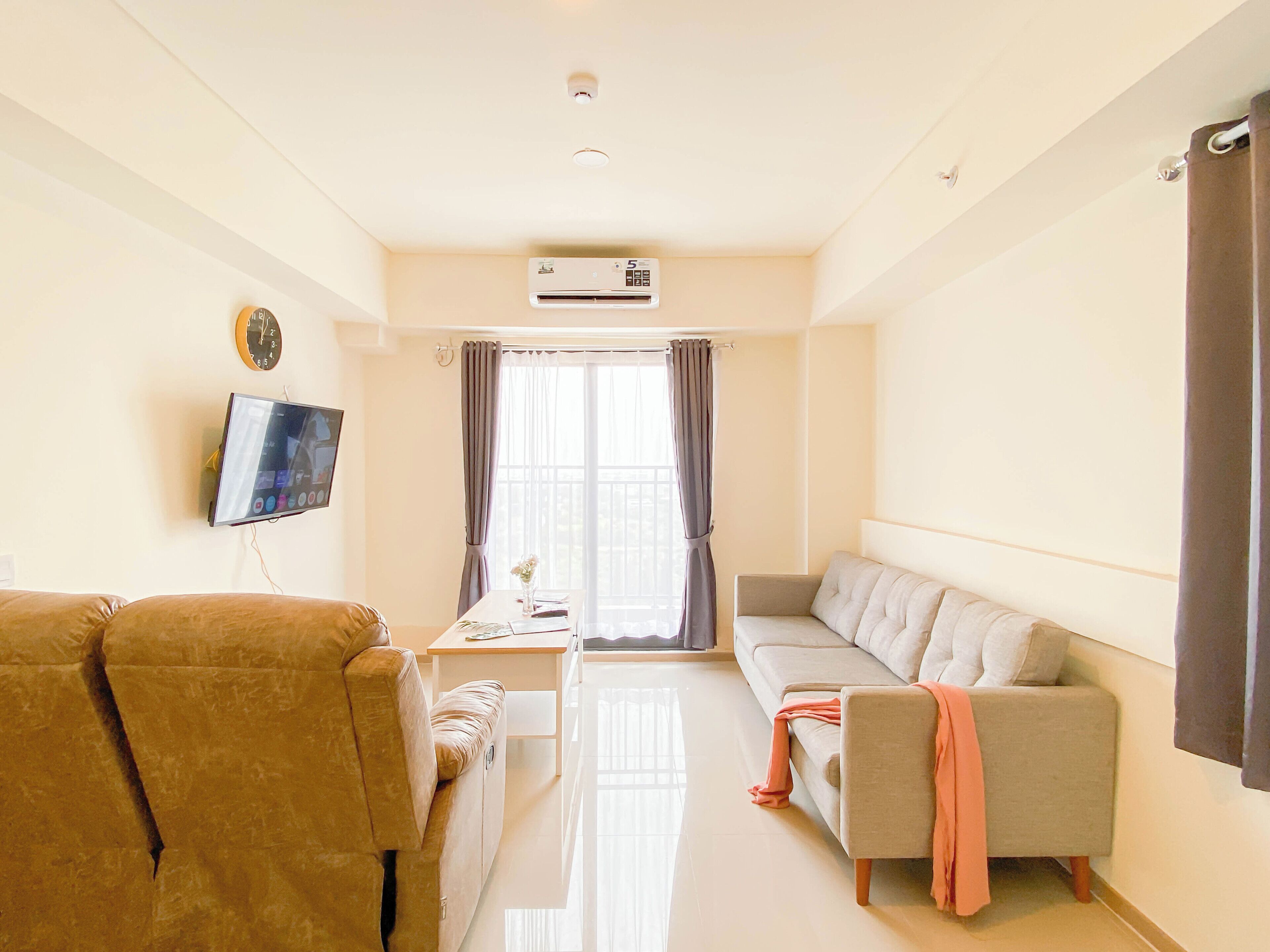 A living room with a sofa, a brown armchair, a flat-screen TV, and a window with curtains.
