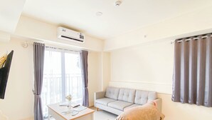 A modern living room with a grey sofa, a white coffee table, and a grey couch. There is a flat-screen TV mounted on the wall, and an air conditioning unit above the sofa.