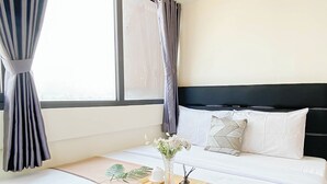 A hotel room with a large window, a bed with white bedding, a tray with a vase of flowers, and a magazine on the bed.