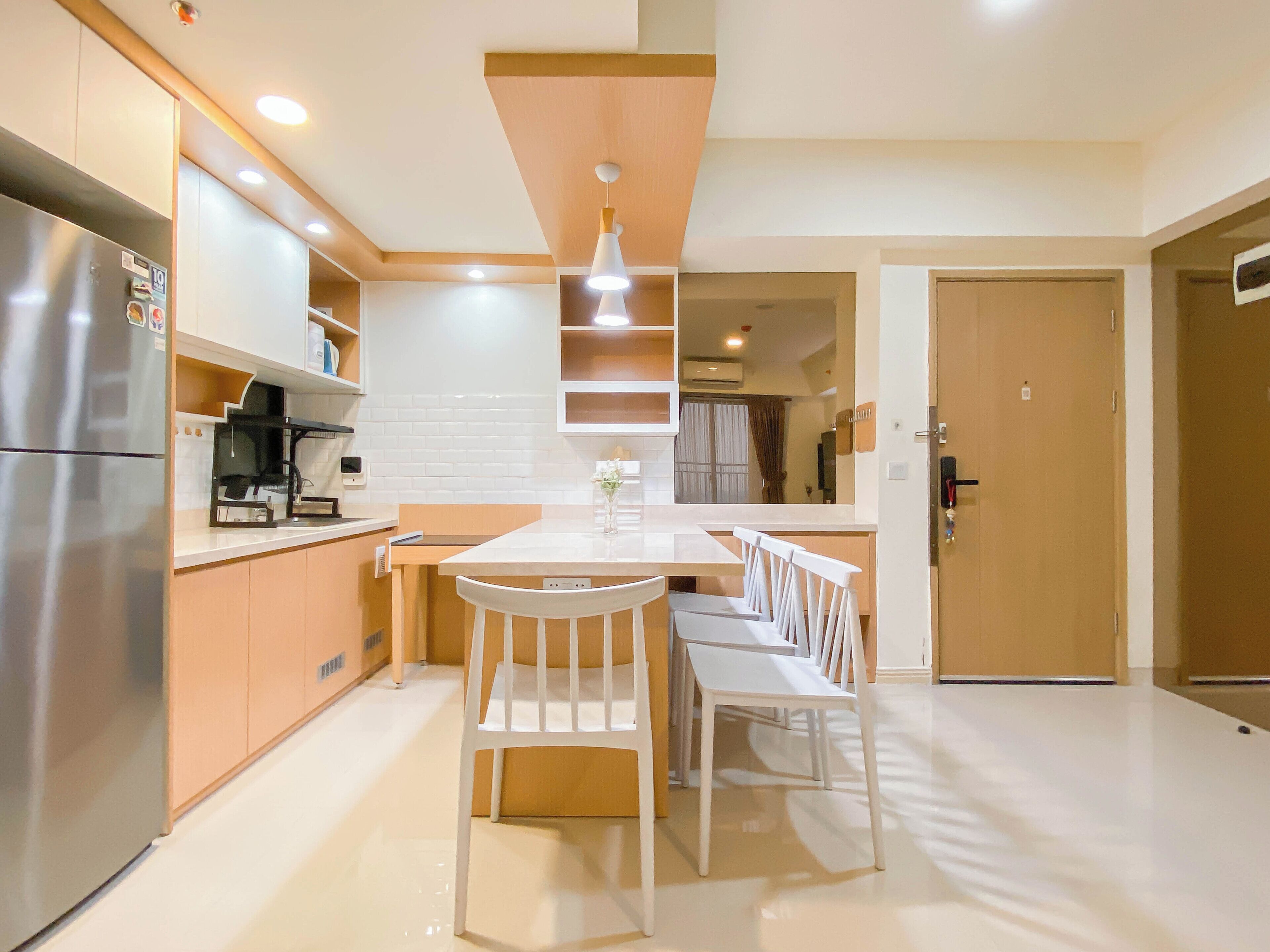 A modern kitchen with a central island, white chairs, and a stainless steel refrigerator.