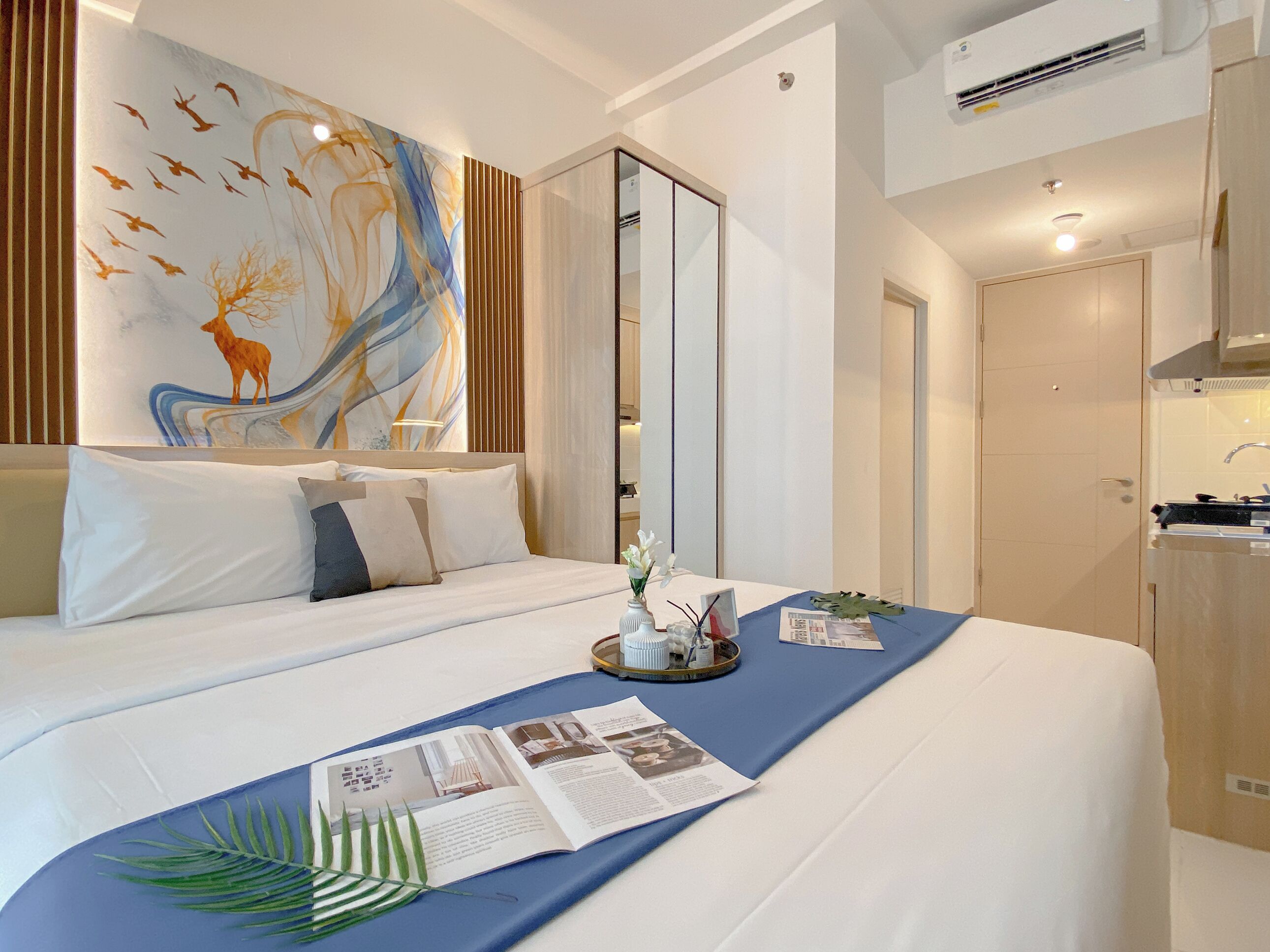 A hotel room with a bed, a bedside table with a magazine, a decorative wall piece, and a view of the bathroom.