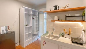 A compact kitchen with white cabinets, a built-in oven, and a sink. There are shelves above the counter holding kitchenware and a small plant. - Good Studio Room at Cinere Resort Apartment (Depok)