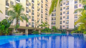 A large indoor swimming pool with clear blue water, surrounded by lush greenery and a multi-story building with balconies. - Good Studio Room at Cinere Resort Apartment (Depok)