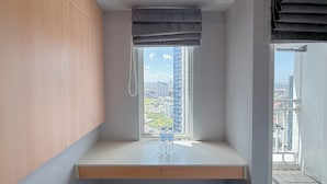 A modern room with a built-in bench, a window with a view of a cityscape, and two water bottles on the bench. - Pleasant and Restful Studio at Orchard Supermall Mansion Apartment (Surabaya)