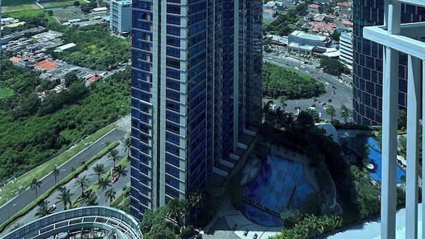 A high-rise building with a modern design, surrounded by greenery and other buildings. - Pleasant and Restful Studio at Orchard Supermall Mansion Apartment (Surabaya)