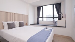 Ein modernes Hotelzimmer mit einem großen Bett, einem Schreibtisch mit Lampe und Blick auf die Stadt durch ein Fenster.