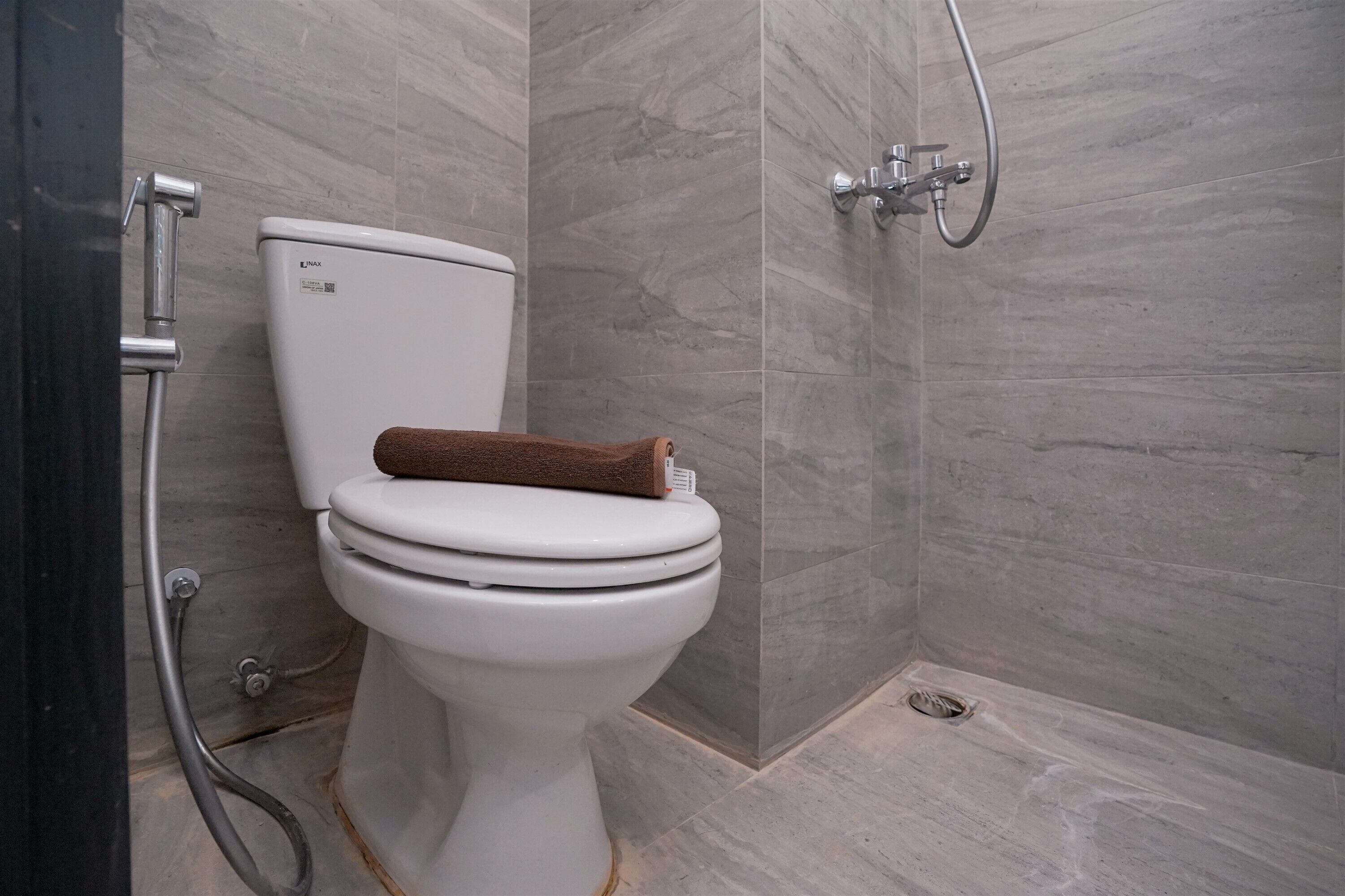 A modern bathroom with a white toilet, a showerhead, and a towel placed on the toilet.