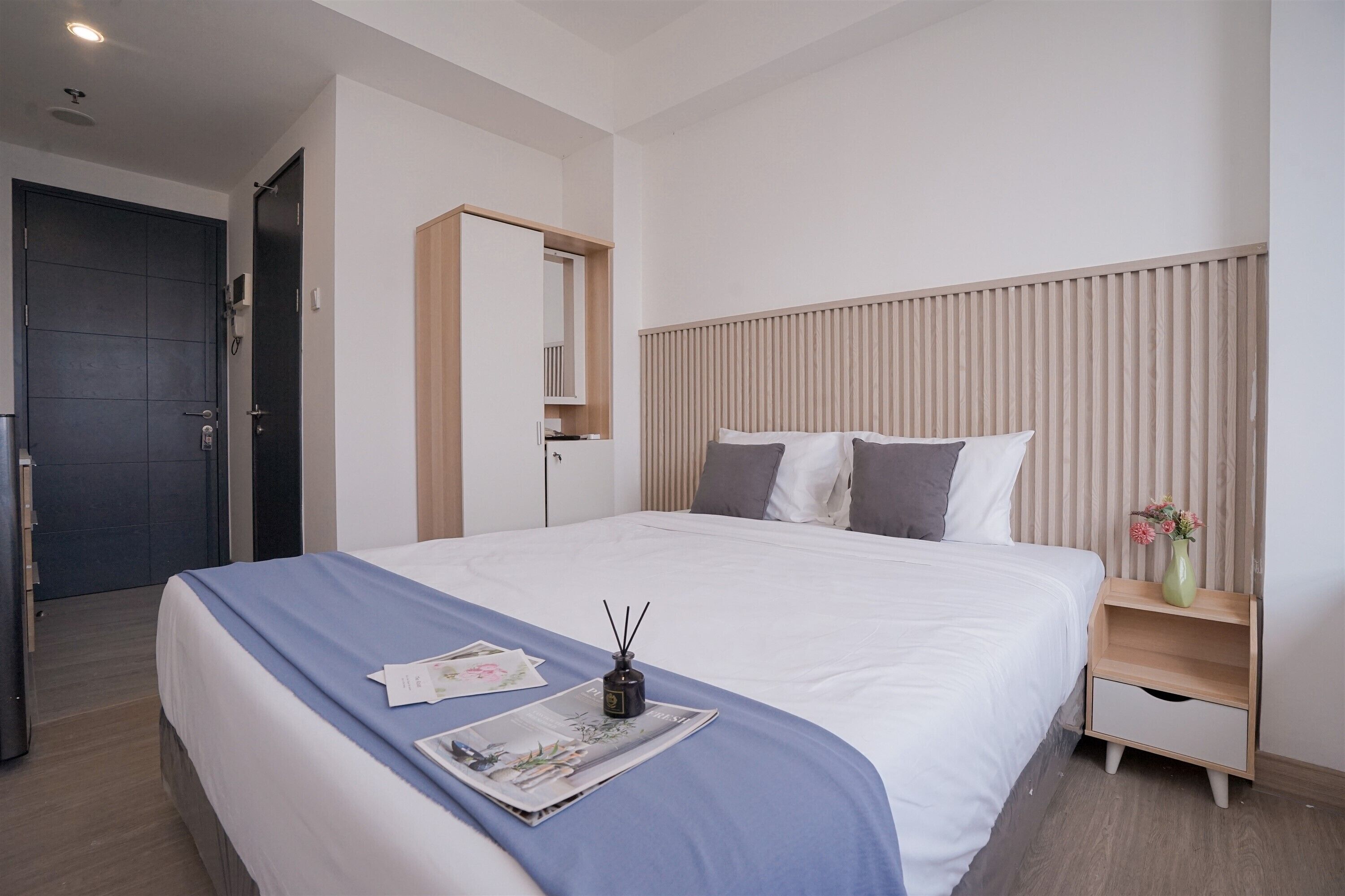 A neatly made bed with a blue bedspread, a bedside table with a vase of flowers, and a wooden headboard.