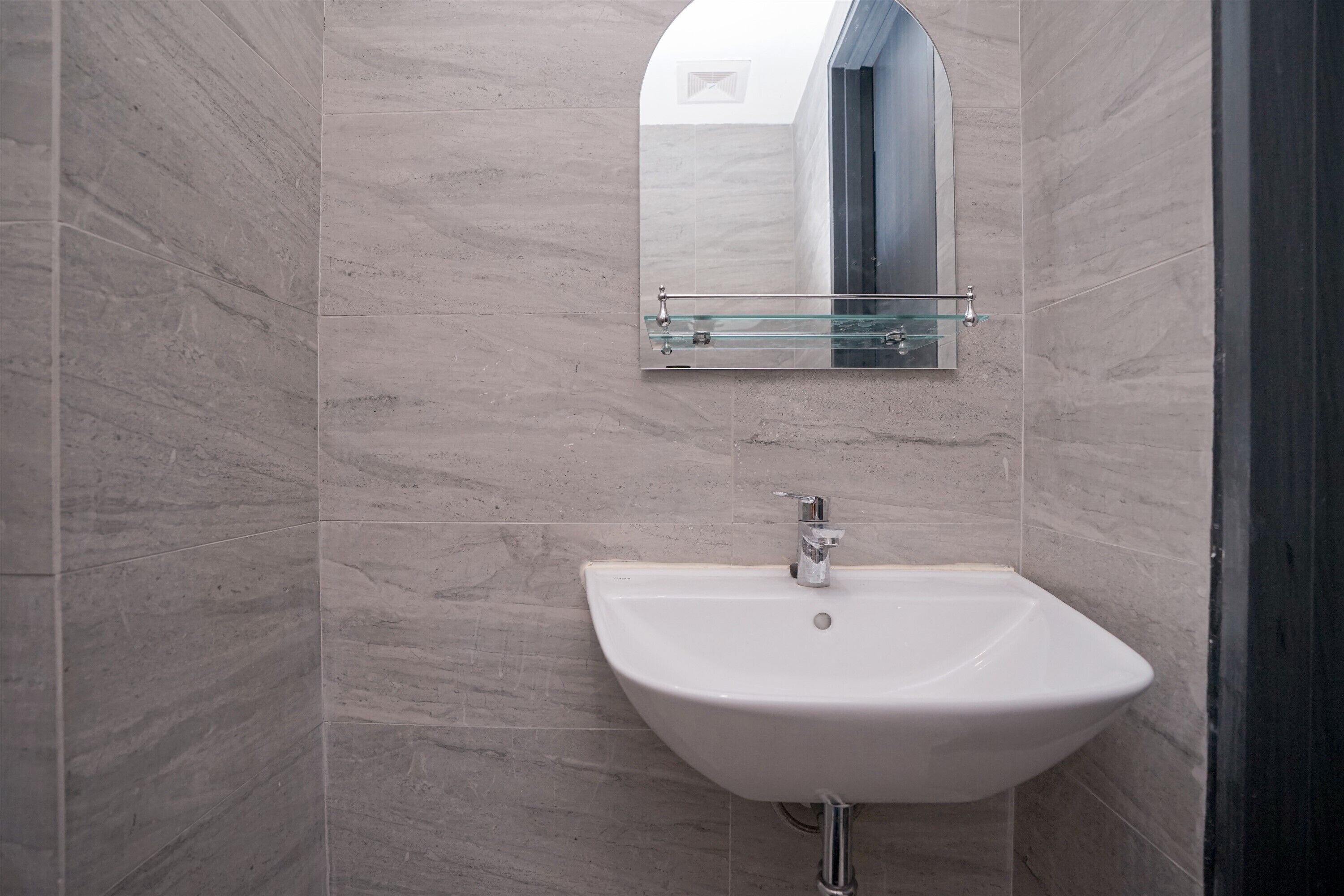A bathroom with a white sink, a glass shelf above it, and a mirror.