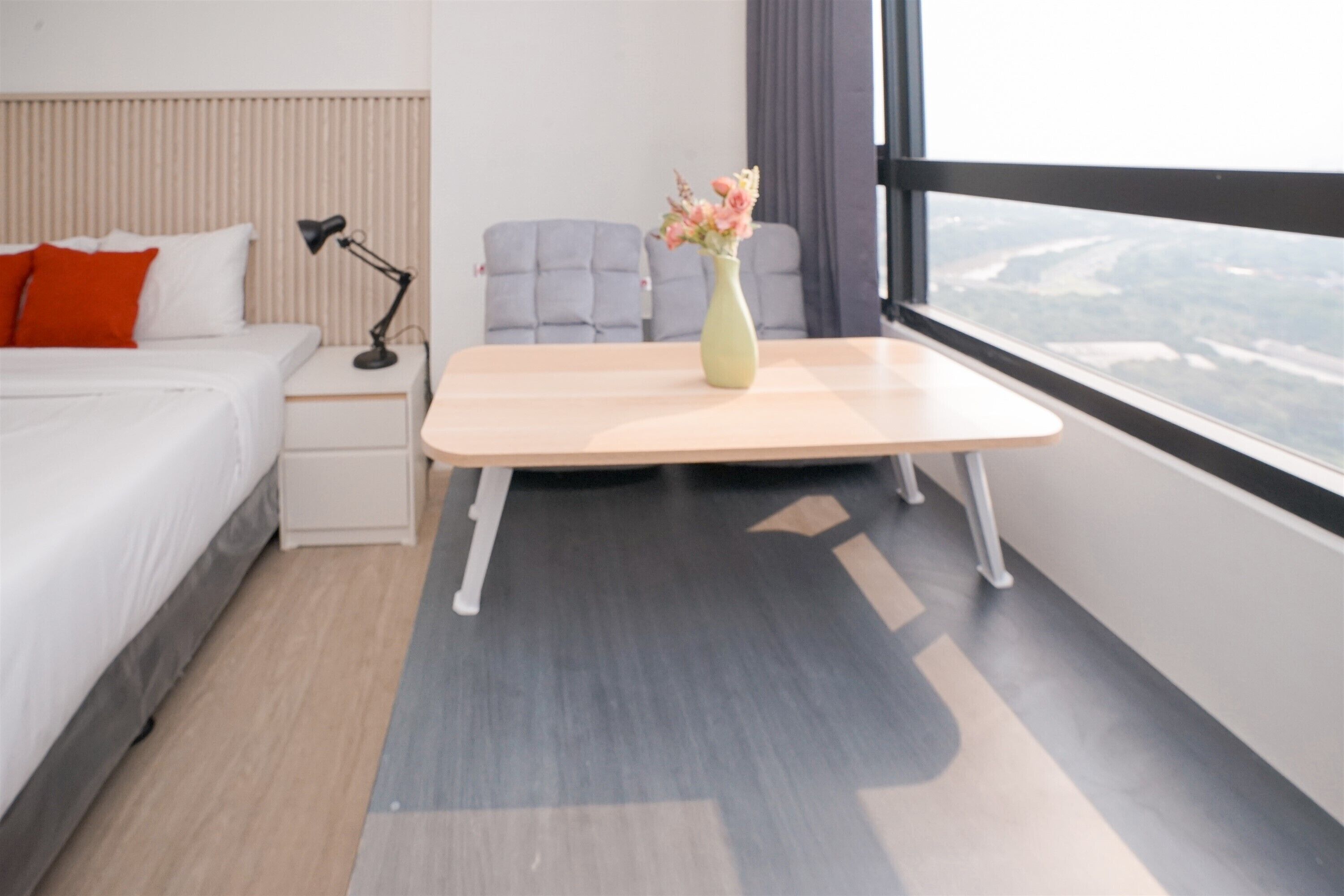 A modern hotel room with a bed, bedside table, lamp, and a vase with flowers.