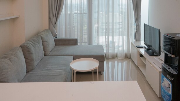 A modern living room with a grey sofa, a small white table, a flat-screen TV, and a coffee machine. - Spacious 1BR at Tree Park City BSD Apartment (South Tangerang)
