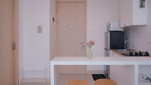 A compact kitchen with a white countertop, two wooden stools, a small sink, and a microwave. - Spacious 1BR at Tree Park City BSD Apartment (South Tangerang)