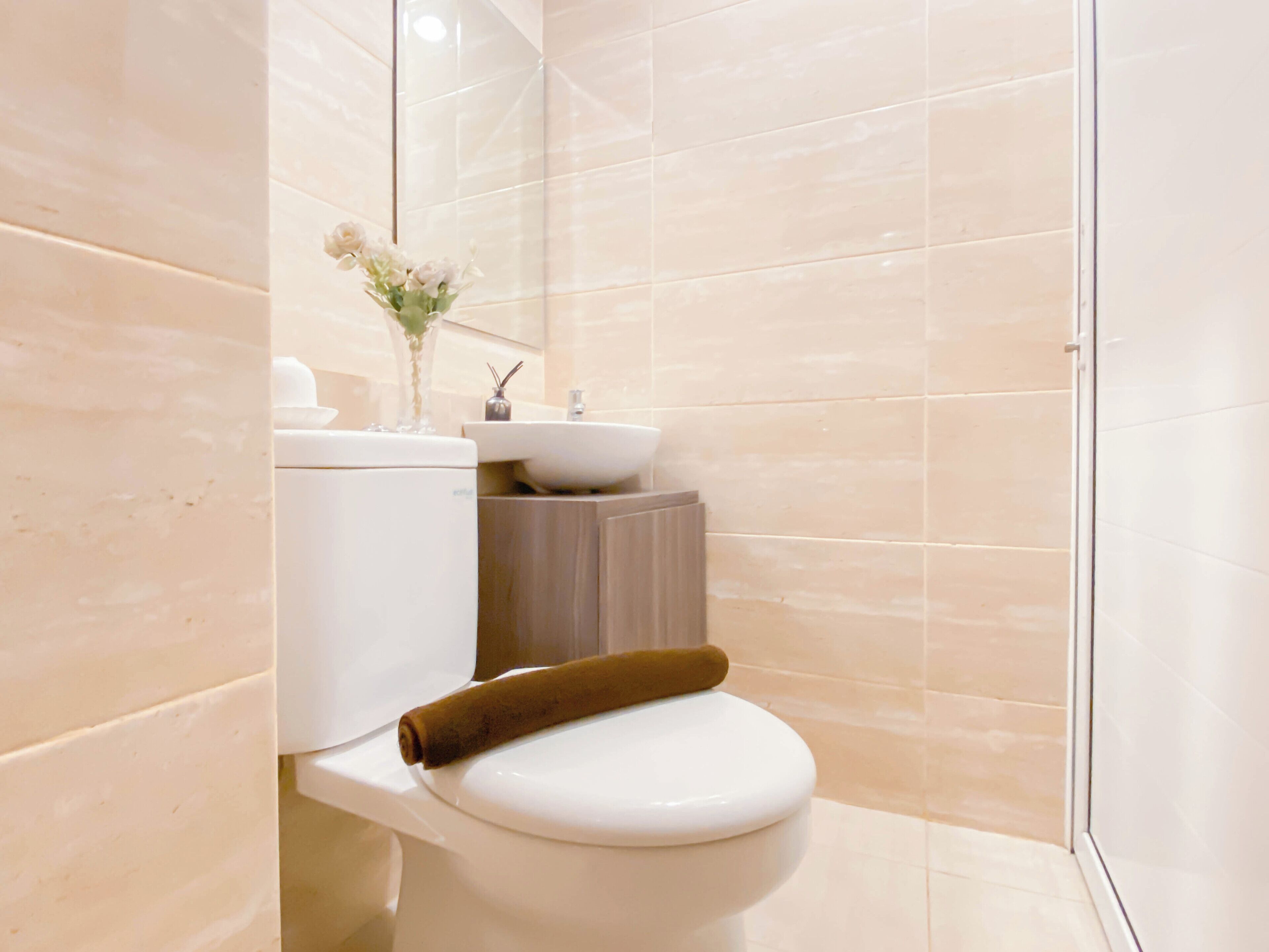 A modern bathroom with a toilet, sink, and a small vase of flowers.