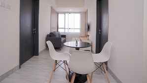 Una habitación moderna con una mesa redonda y cuatro sillas blancas, un sofá gris y un televisor montado en la pared.