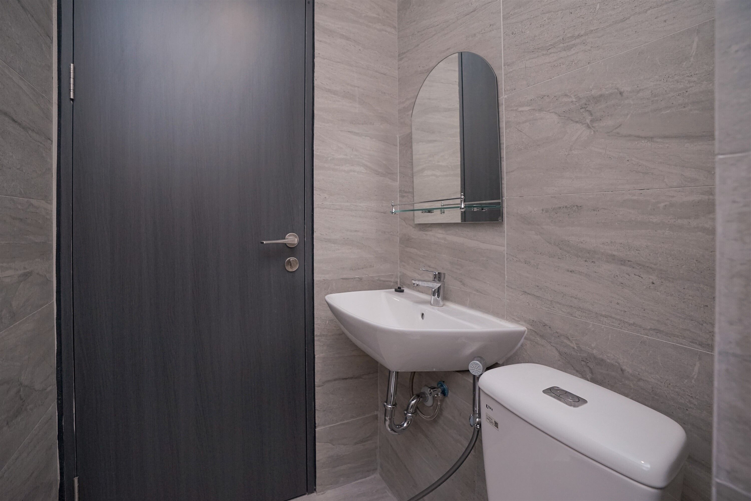 A bathroom with a dark wooden door, a white sink with a mirror above it, and a white toilet.
