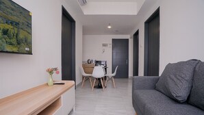 Una sala de estar moderna con un sofá gris, una mesa consola de madera con un jarrón, y un comedor con una mesa y sillas blancas.
