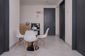 A compact kitchen with a dining area, featuring a small table and chairs, a kettle, and a coffee machine.