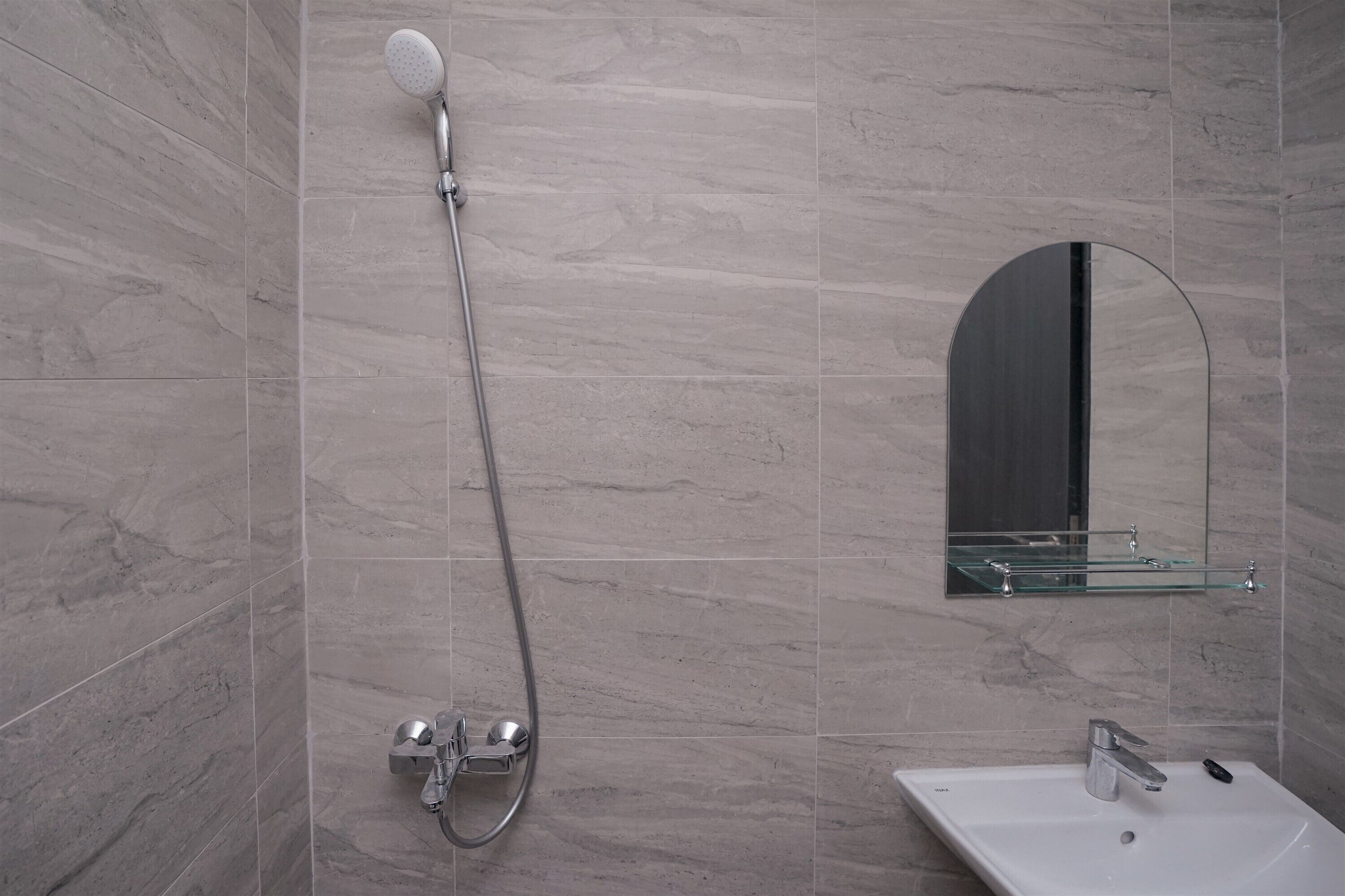 A bathroom with a shower, a sink, and a glass shelf above the sink.