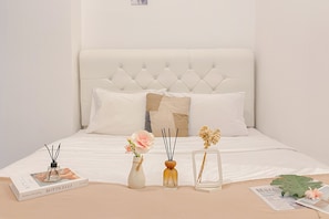 A neatly made bed with a tufted headboard, white bedding, and a few decorative items including a book, vases, and a framed picture. - Stunning Studio Room at Tokyo Riverside PIK 2 Apartment (Teluknaga)