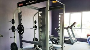 Un gimnasio con una zona de levantamiento de pesas, una cinta de correr y un ventanal con vistas a zonas verdes.