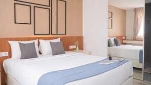 Una habitación de hotel con una cama grande, una cama más pequeña, una mesita de noche con un florero y un espejo.