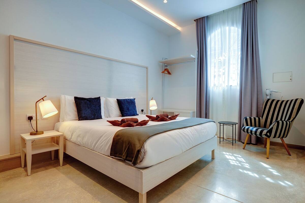 Een moderne hotelkamer met een groot bed, nachtkastjes, een stoel en een raam met gordijnen.