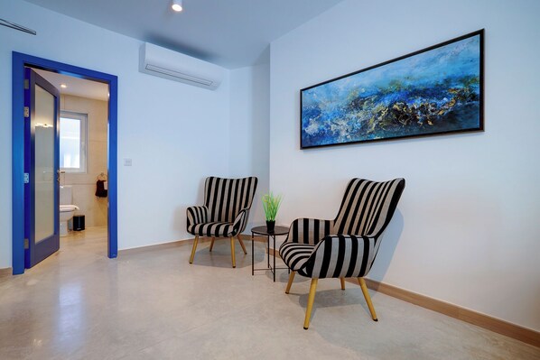 Un hall d’hôtel moderne avec deux fauteuils à rayures, une petite table sur laquelle est posée une plante, et un grand tableau abstrait accroché au mur.