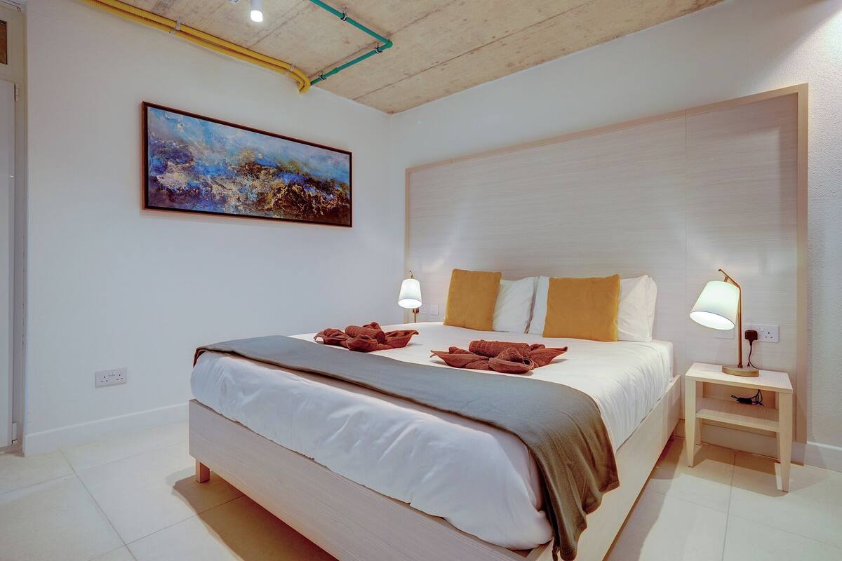 Een moderne hotelkamer met een groot bed, twee bedlampen, een schilderij aan de muur en een klein nachtkastje.
