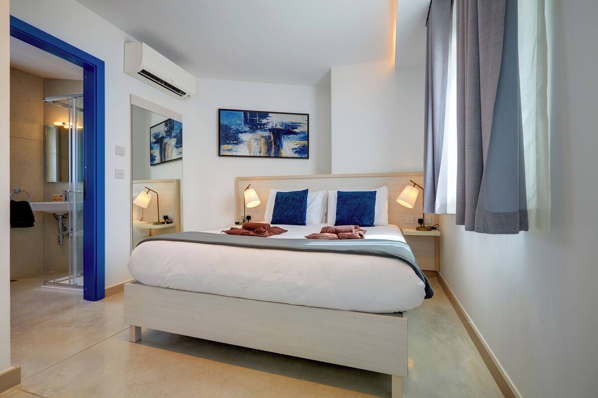 Een moderne hotelkamer met een groot bed, bedlampen, een badkamer met een wastafel en spiegel, en kunstwerken aan de muur.