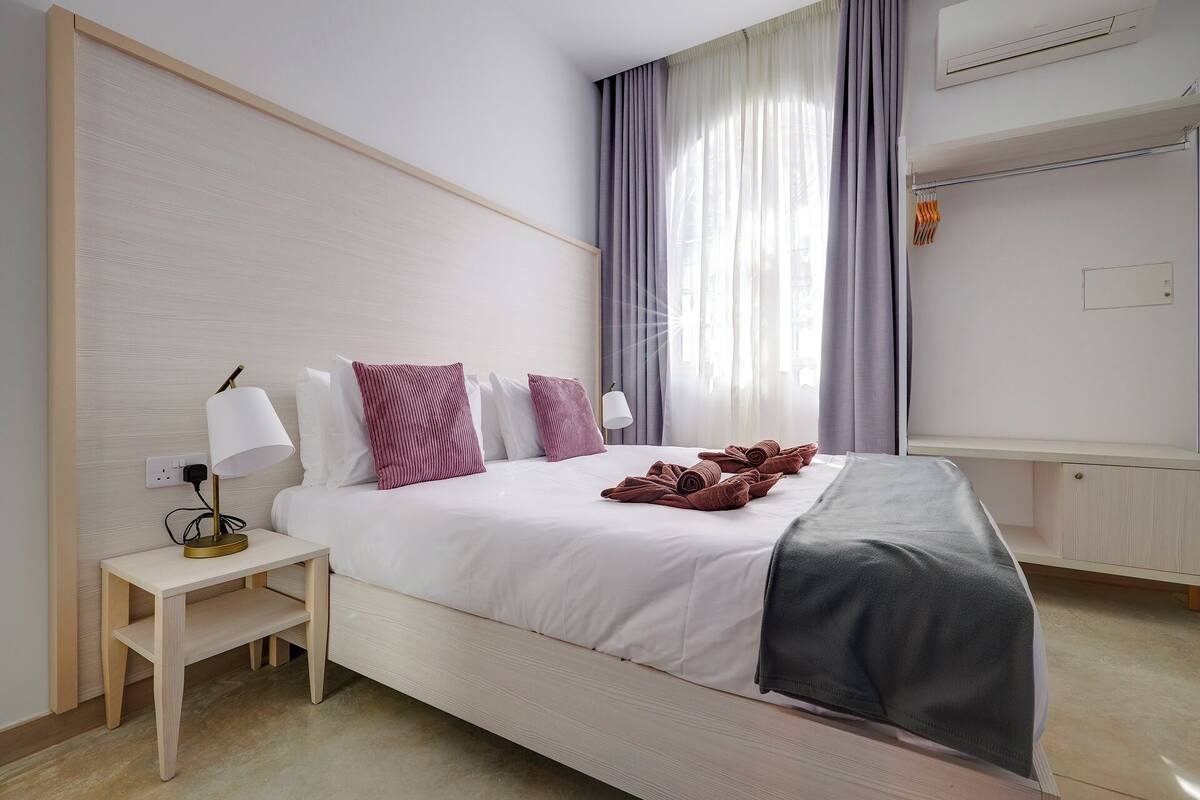 Een hotelkamer met een bed, nachtkastje, lamp en een raam met gordijnen.
