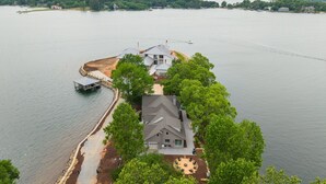 A large house with a dock extending into a lake, surrounded by trees.