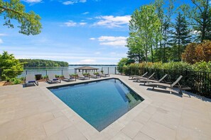 A rectangular swimming pool with lounge chairs and a gazebo, surrounded by a landscaped garden and a view of a lake. - Stone Point Overlook w/Optional Boat Rental (Mooresville)