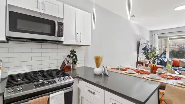 A modern kitchen with white cabinets, a built-in microwave, a gas stove, and a dining area with a table set for two.