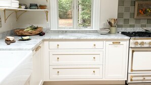 A kitchen with white cabinetry, a marble countertop, a window with a view of greenery, and a patterned rug on the floor. - 6bedroom, 4bath, chefs kitchen, central air, ping pong, walking distance to town (Tisbury)