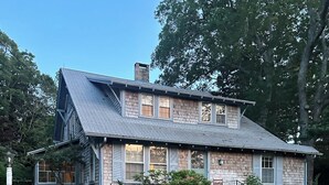 A two-story house with a sloped roof, a front porch, and a stone chimney. - 6bedroom, 4bath, chefs kitchen, central air, ping pong, walking distance to town (Tisbury)