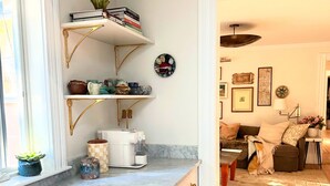 A modern kitchen with white cabinetry, gold handles, and a marble countertop. There are shelves above the counter holding books and decorative items. - 6bedroom, 4bath, chefs kitchen, central air, ping pong, walking distance to town (Tisbury)