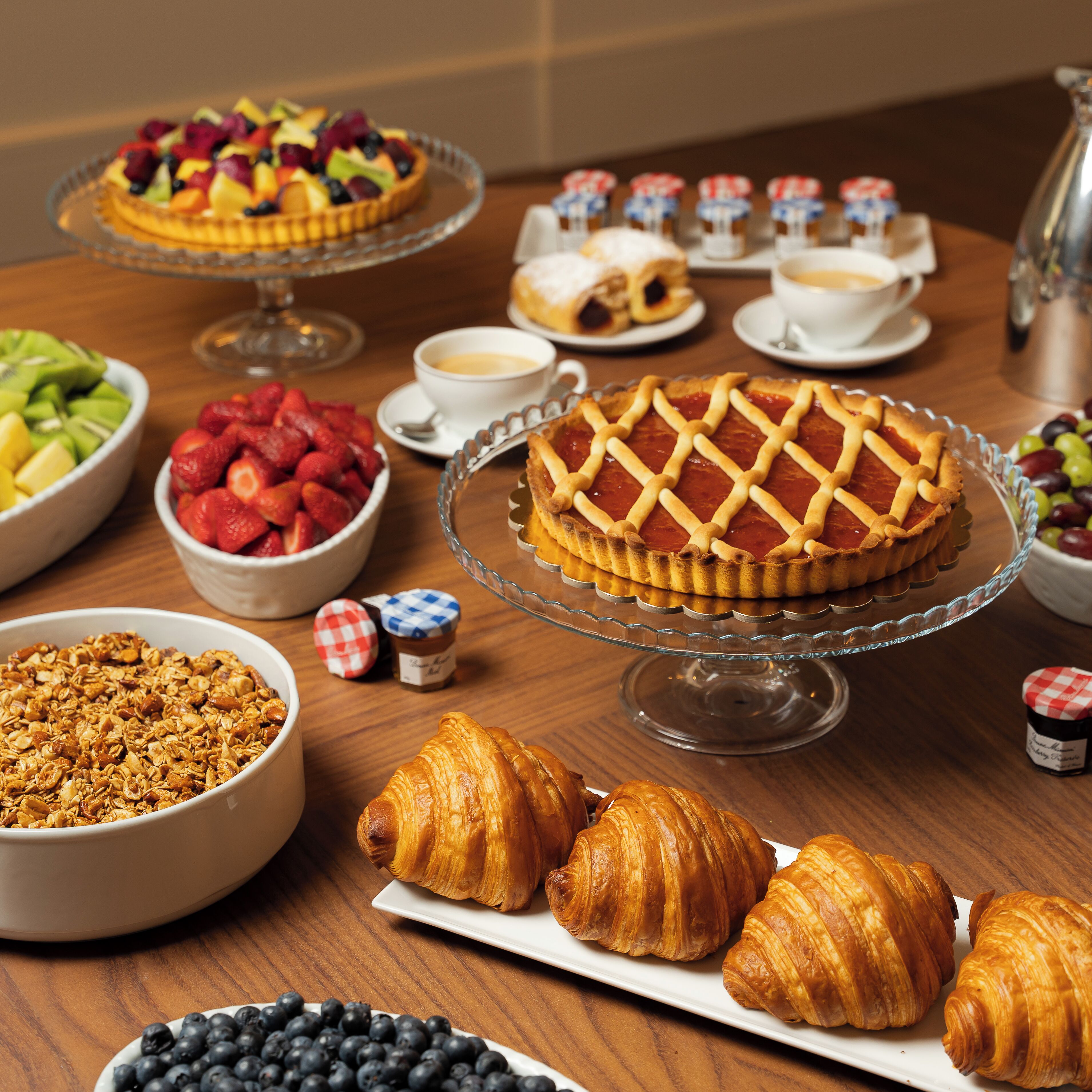 Un bufé de desayuno con diversas opciones de comida, incluyendo una tarta de frutas, pastelería, croissants y un pastel.
