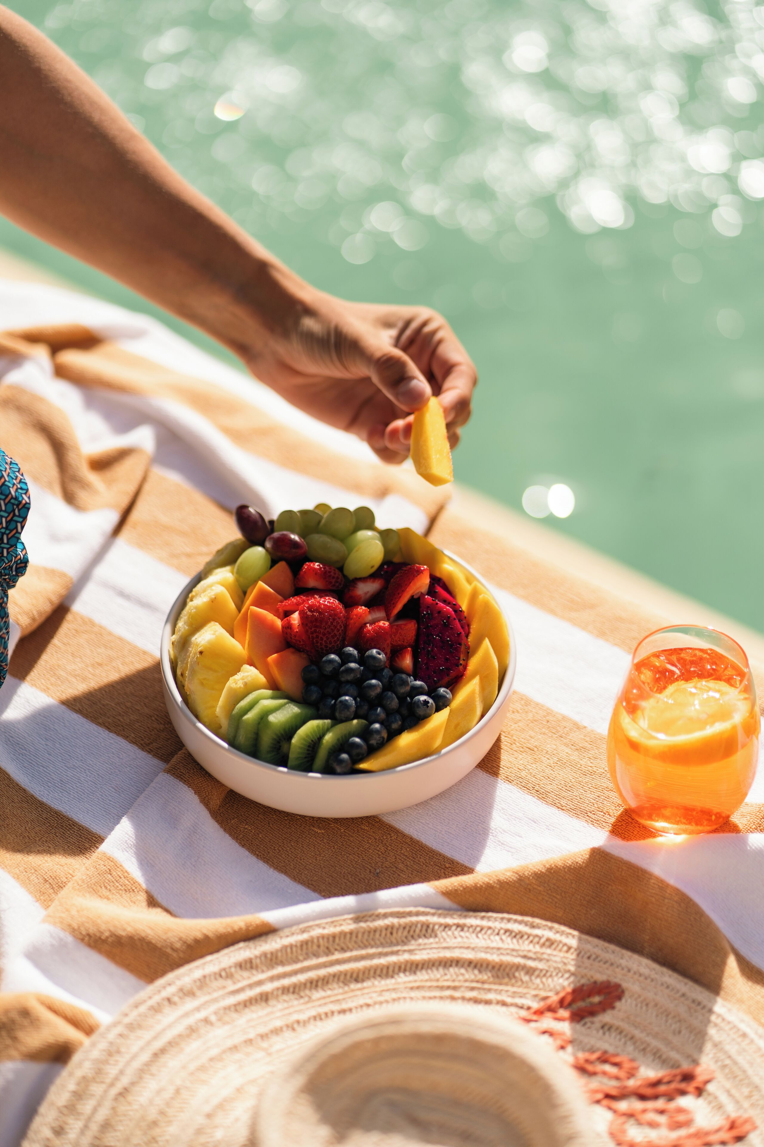 A bowl of fruit on a table with a drink beside it.