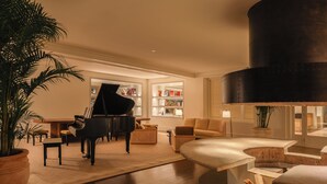A spacious living room with a grand piano, a comfortable sofa, a coffee table, and a bookshelf filled with books. - Locanda Punta del Este (Punta del Este)