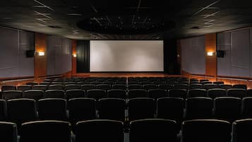 A movie theater with rows of seats, a large screen, and wall-mounted speakers.