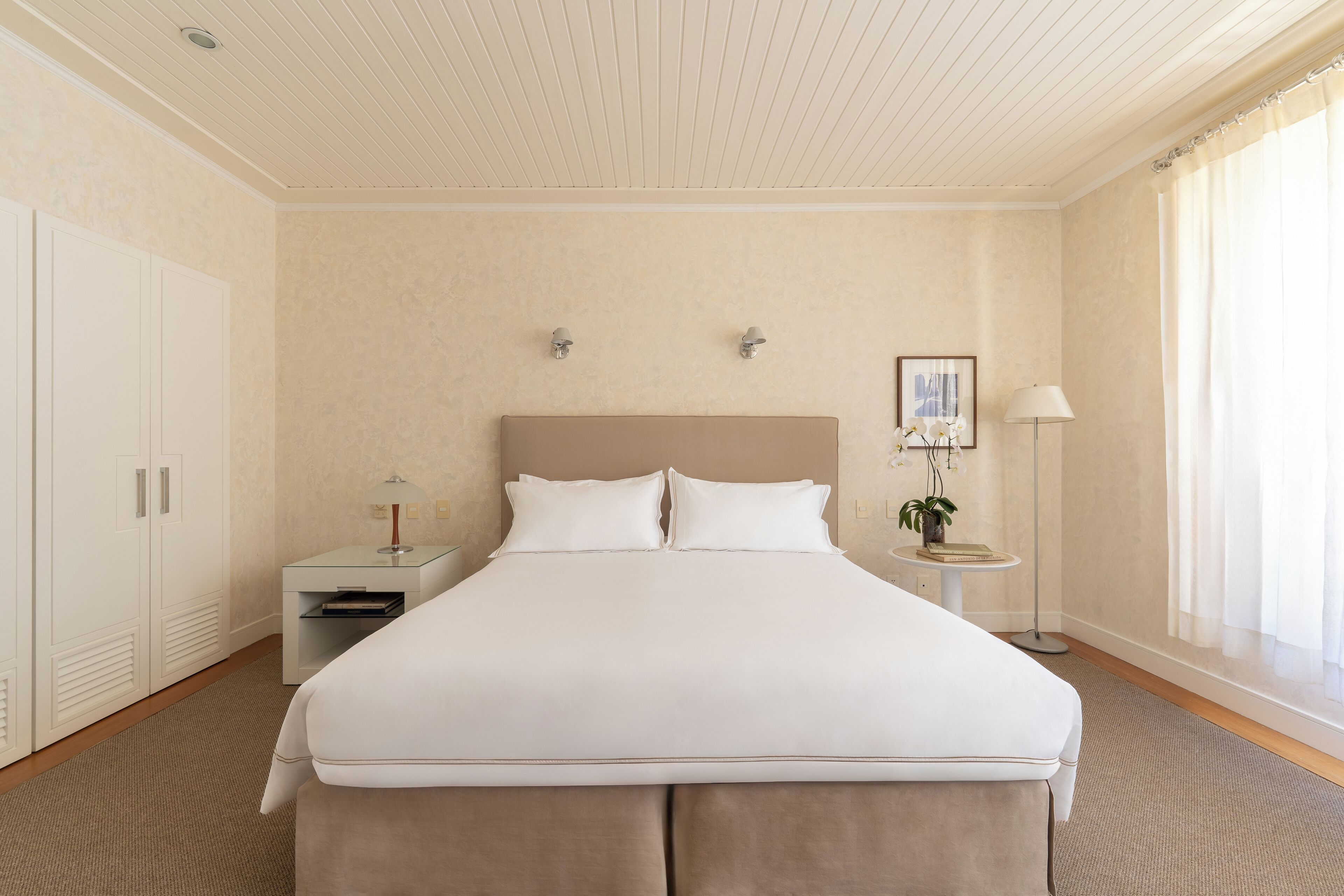 Habitación de hotel ordenada con una cama grande, mesitas de noche, una lámpara y un ventanal con cortinas.