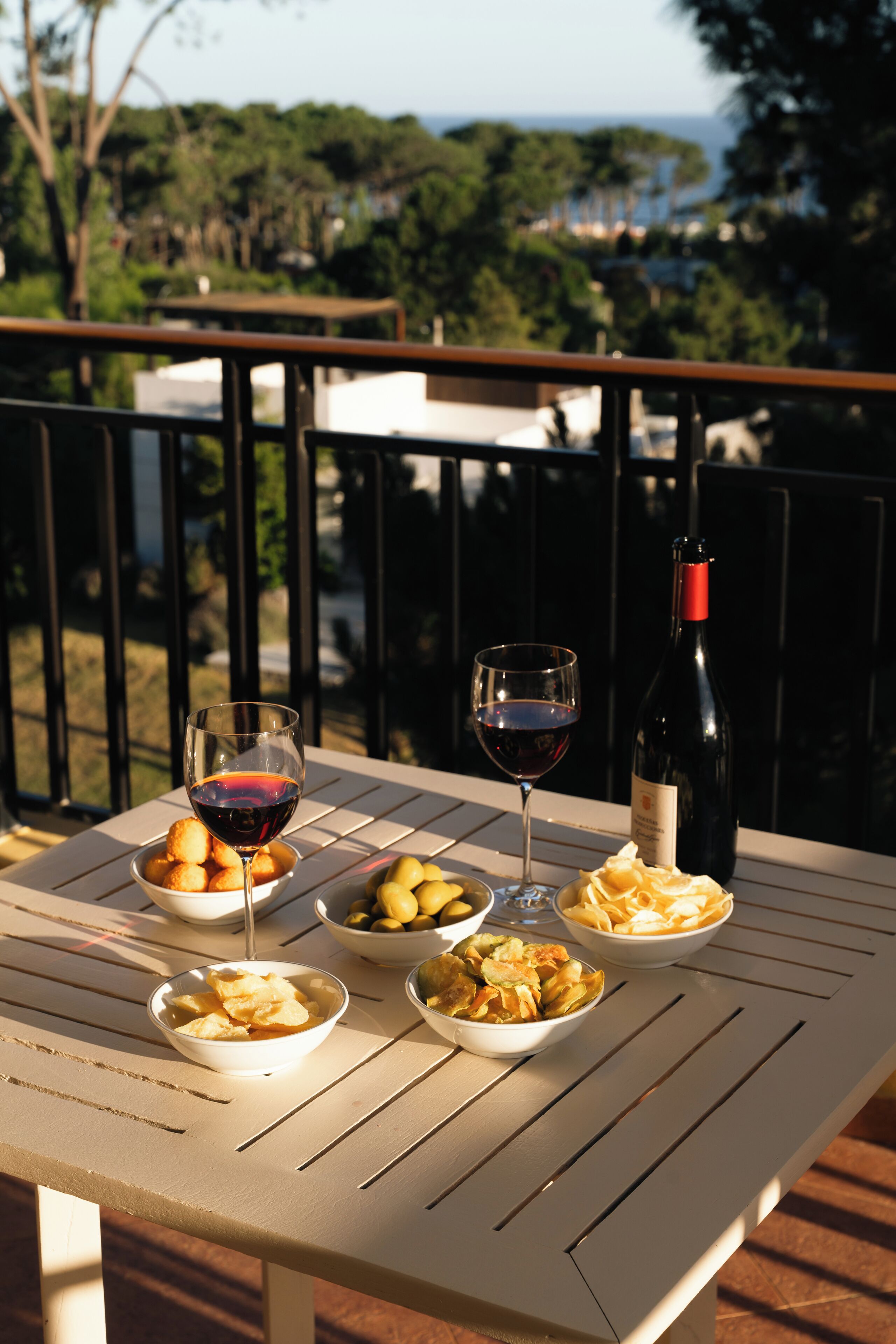 A table with plates of food and wine glasses on a balcony overlooking a scenic view.