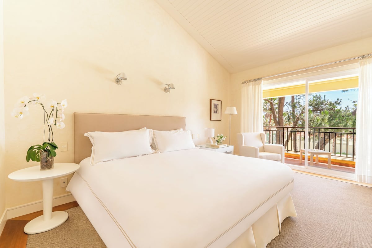 Ein geräumiges Schlafzimmer mit einem großen Bett, einem kleinen Nachttisch, einem Beistelltisch, einem Sessel und einem Balkon mit Geländer.