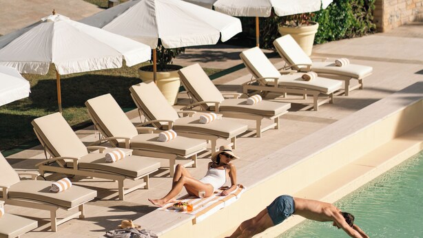 A poolside area with lounge chairs and umbrellas, a diving board, and a clear pool. - Locanda Punta del Este (Punta del Este)