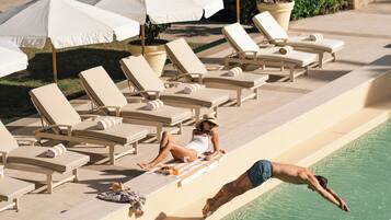 Una piscina al aire libre, sombrillas, sillones reclinables de piscina
