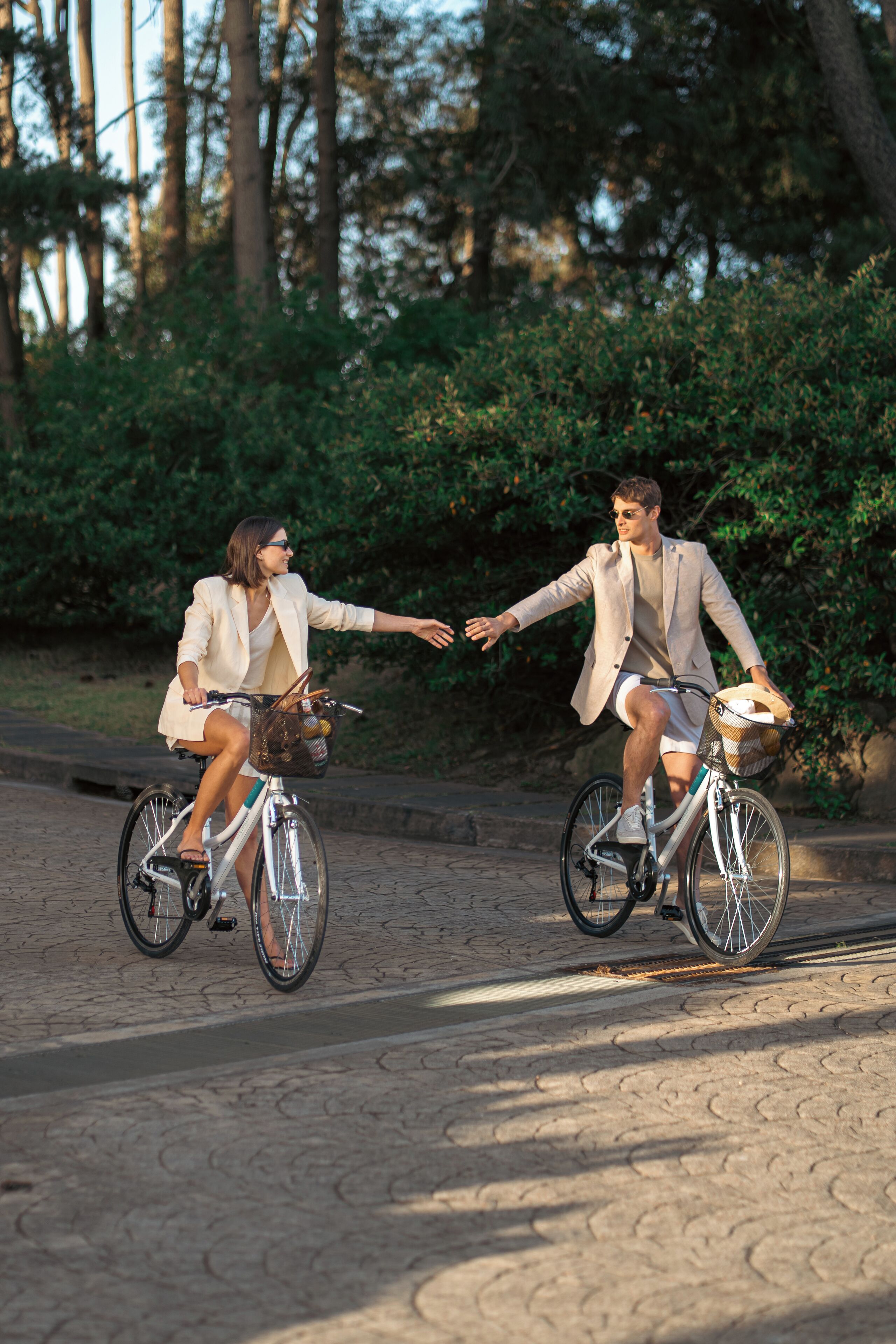 Two people riding bicycles on a paved path with greenery in the background.
