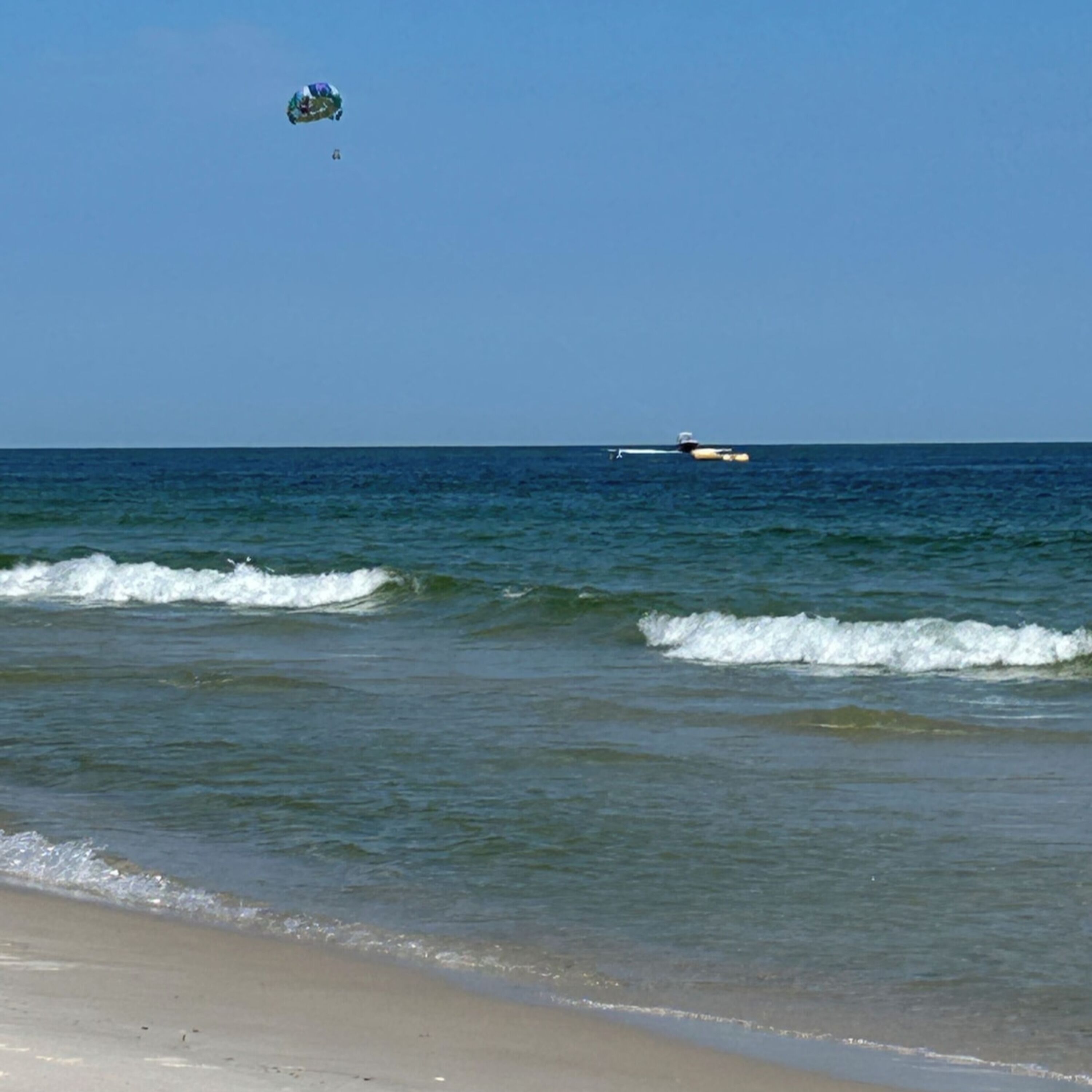 A beach with waves, a boat, and a kite in the sky.